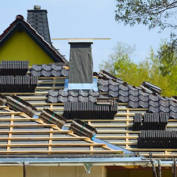 New tiled roof installation underway by Roofing Guys Sydney, showing roof battens, stacked tiles, and chimney flashing in progress.