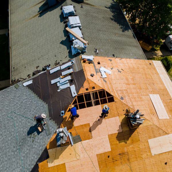 Roofing Guys Sydney crew installing a new roof during a home renovation project, showing exposed timber sheeting and partial shingle coverage.