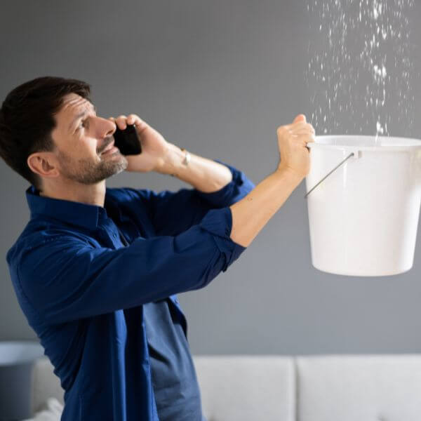 Worried business owner catching water from a ceiling leak with a bucket while calling Roofing Guys Sydney, experts in fast commercial roof leak detection and repairs across Sydney Worried business owner catching water from a ceiling leak with a bucket while calling Roofing Guys Sydney, experts in fast commercial roof leak detection and repairs across Sydney